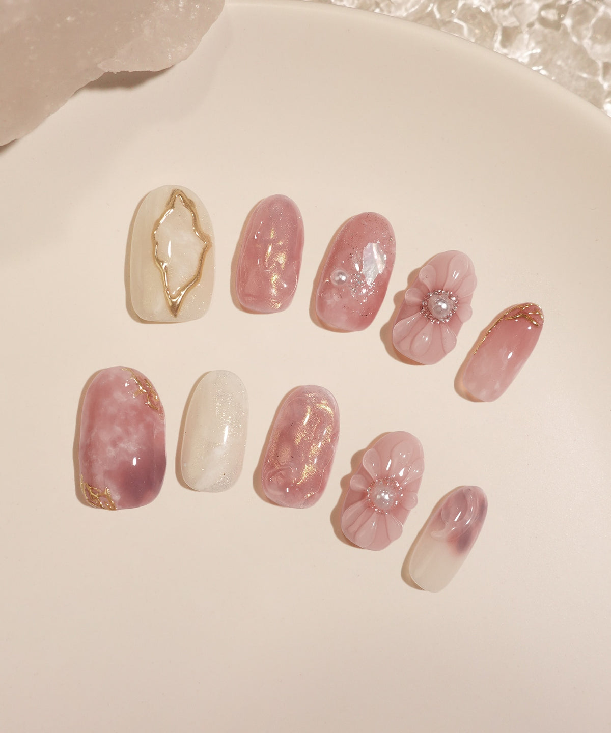 透明感のあるピンクと白を基調に立体的なぷっくりフラワーやゴールドのミラーラインを施したオーバルネイルチップ。両手10本分が白いプレートに並べられています。