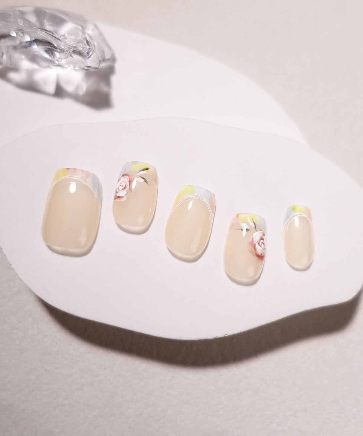 透明感あるベージュをベースにカラフルなフレンチと繊細な薔薇アートを施した、5本並びのショートスクエアネイルチップ。