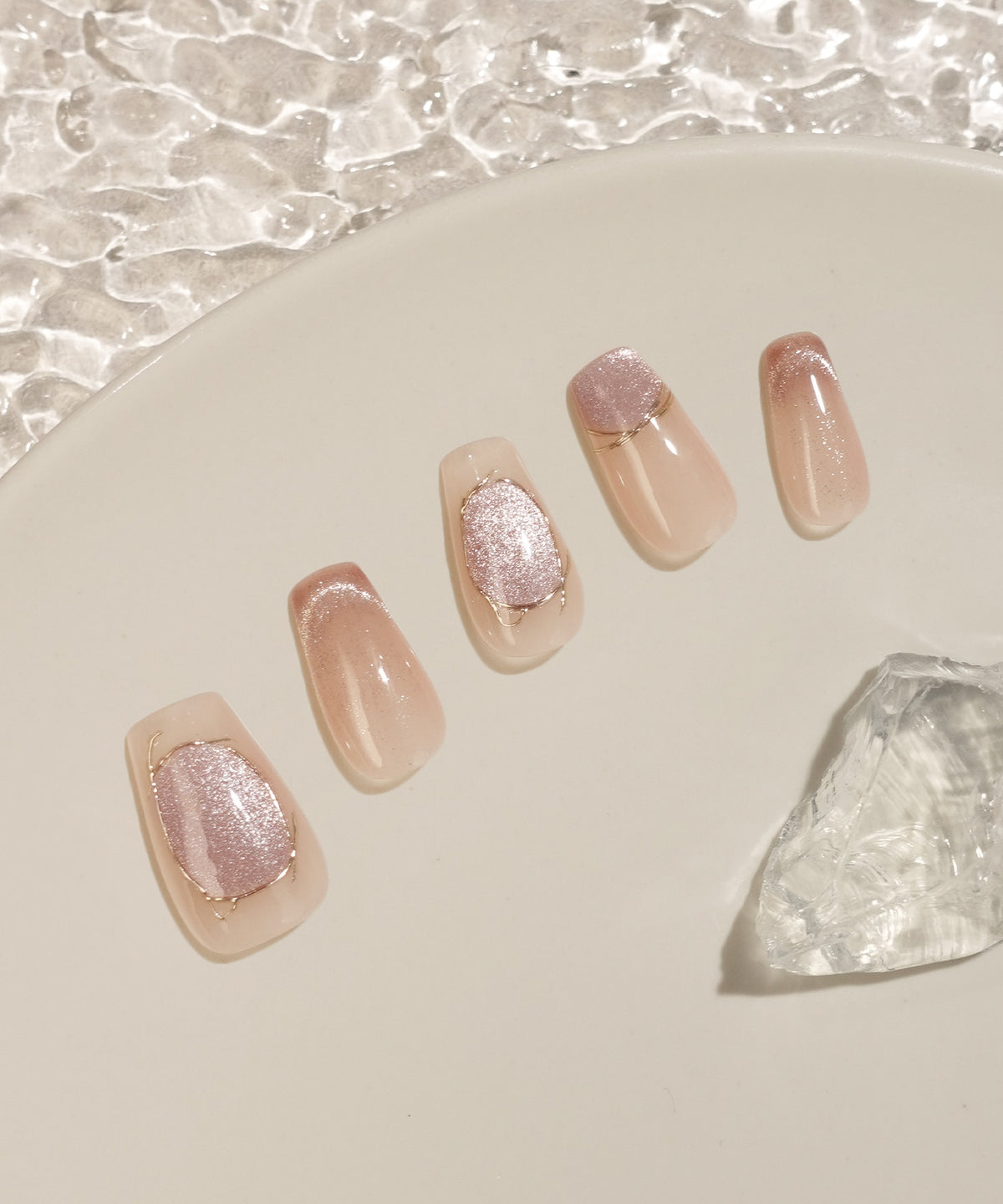 淡いベージュとピンクマグネットにゴールドラインを施したバレリーナネイルチップが、白いプレートの上に並べられています。