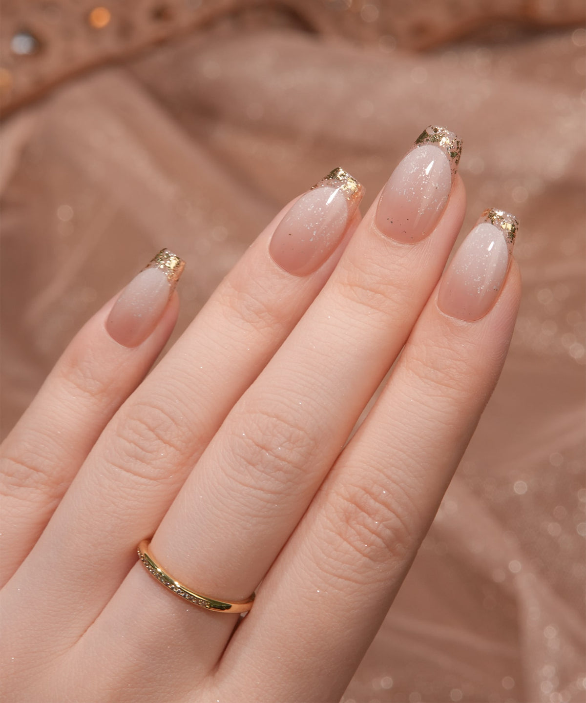 ピンクグラデーションに爪先のゴールドガラスフレンチが輝くバレリーナネイルチップを手に着用した様子。金色の指輪を添えて上品な手元を演出。