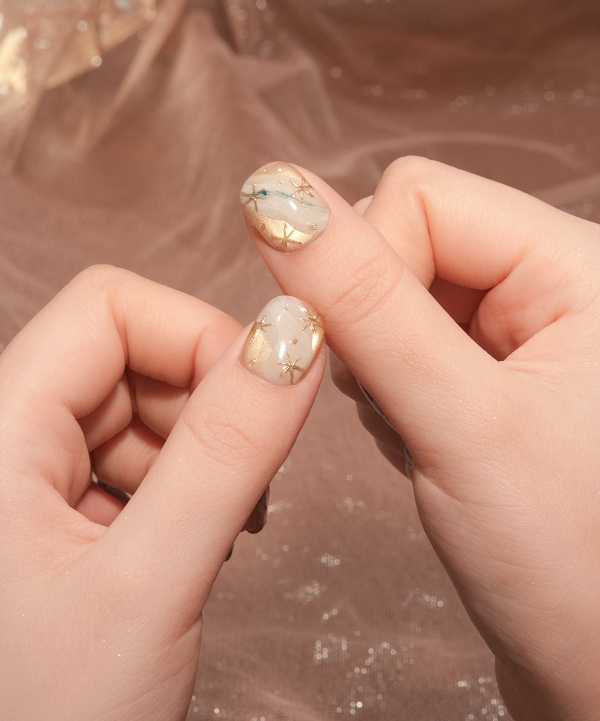 乳白色ベースにゴールドの星モチーフとミラーアートを施した親指用のショートラウンドネイルチップの手元アップ