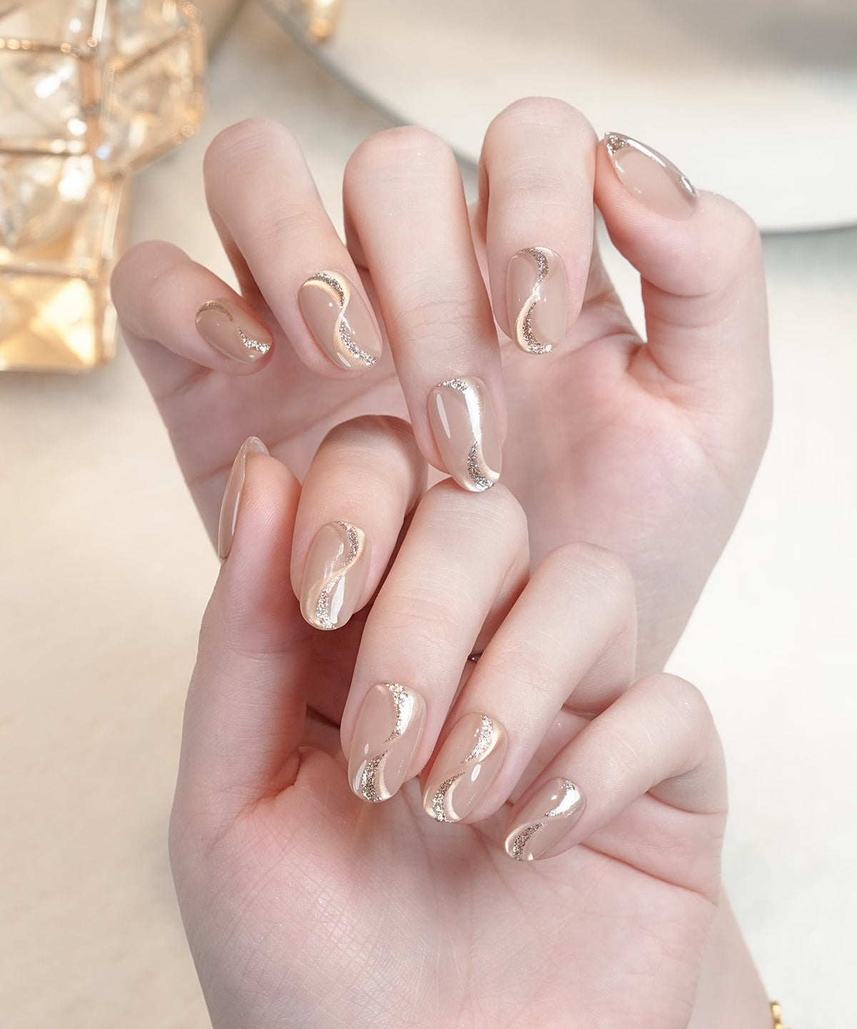 水光感のあるベージュマグネットにシルバーのウェーブラインが描かれたオーバルネイルチップを両手に付けた様子。